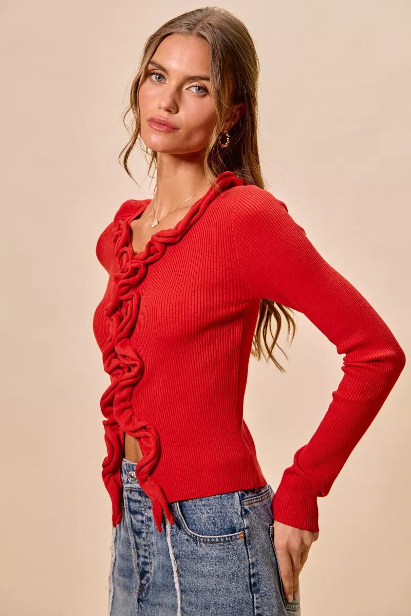 Red ribbed knit cardigan with cascading ruffles, fitted silhouette, denim pairing.
