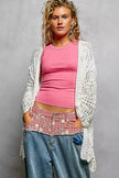 White openwork cardigan with scalloped edge, lightweight knit, loose fit over pink top.