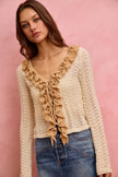 Cream pointelle knit cardigan with ruffled neckline and tie detail.