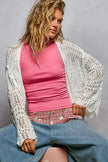 White openwork cardigan with scalloped edges, worn over pink top and jeans.