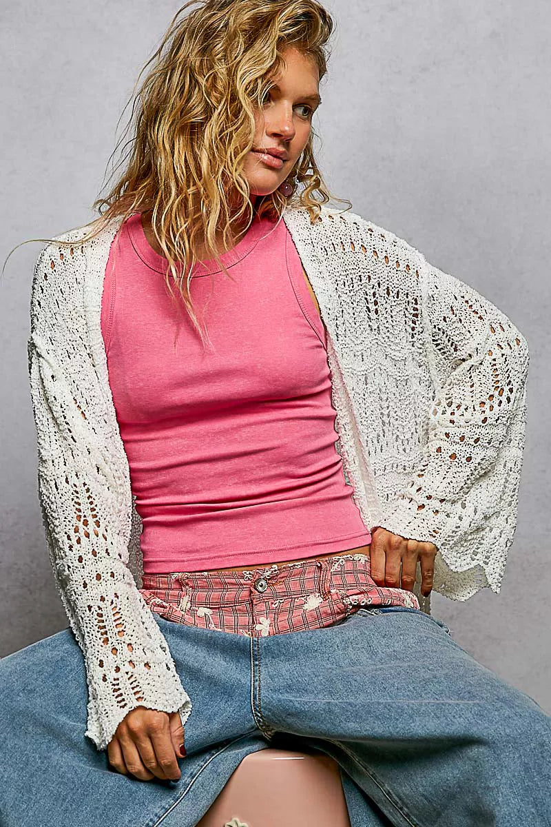 White openwork cardigan with scalloped edges, worn over pink top and jeans.
