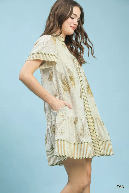 Tan linen dress with gold fern print, button-front, tiered skirt, side pockets, and striped trim.