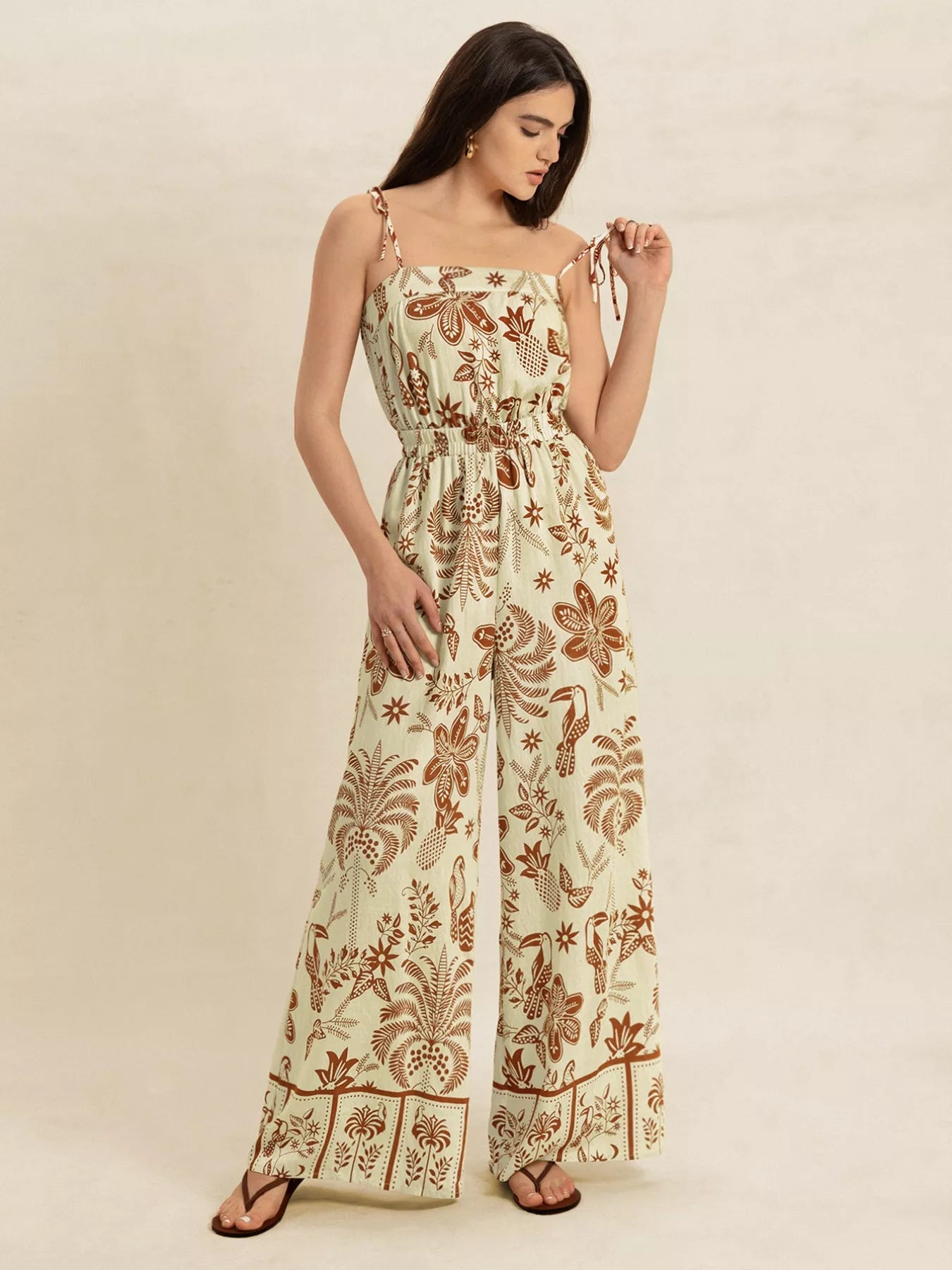 Cream base jumpsuit with brown tropical print, wide legs, tie straps, smocked waist
