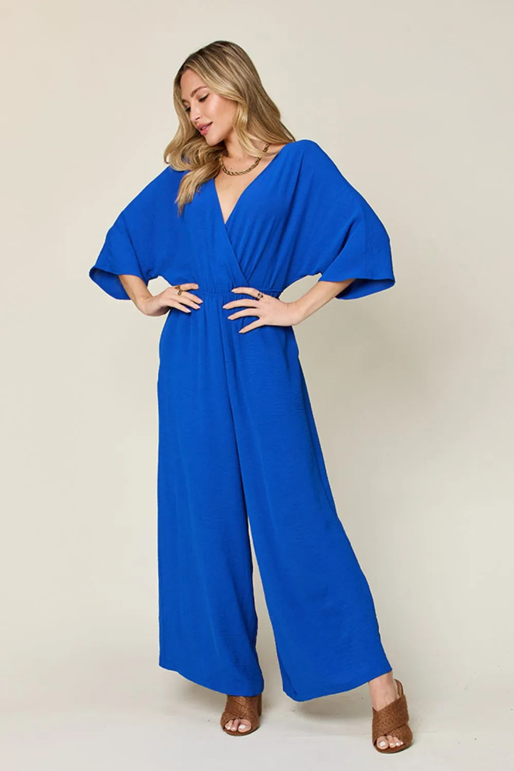 A person poses against a plain background wearing the Rayon Spaghetti-Strap Wide-Leg Jumpsuit with pockets, styled for comfort and ease, paired with brown heeled sandals.