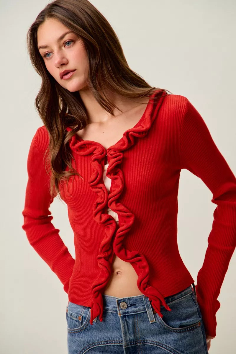 Red ribbed knit cardigan with cascading ruffles, fitted waist, and denim pairing.