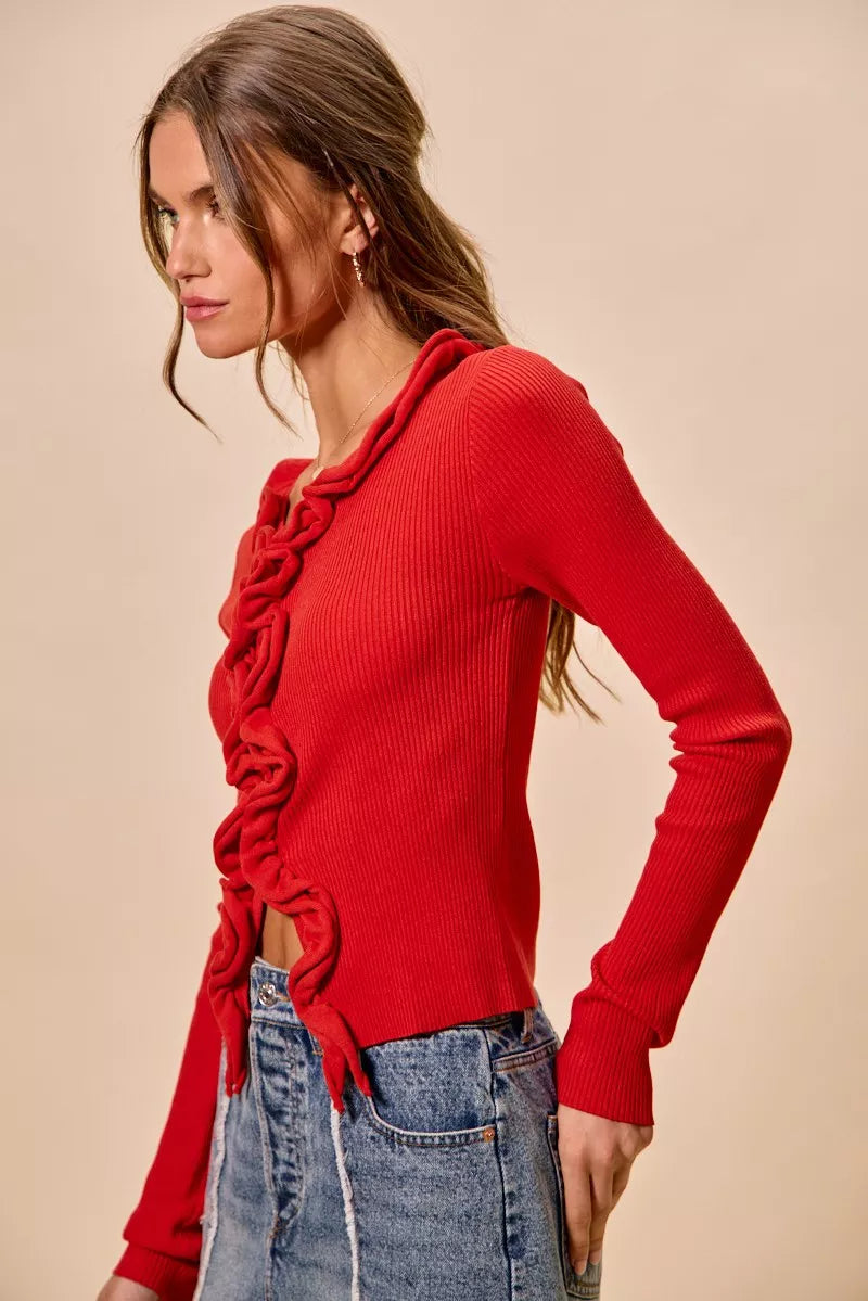 Red ribbed sweater with cascading ruffles, fitted silhouette, denim pairing.