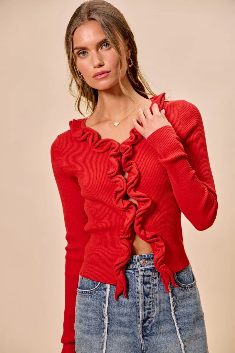 Red ribbed knit cardigan with cascading ruffles, fitted silhouette, denim pairing.