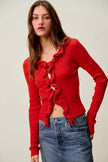 Red ribbed knit cardigan with cascading ruffles, fitted silhouette, denim pairing.