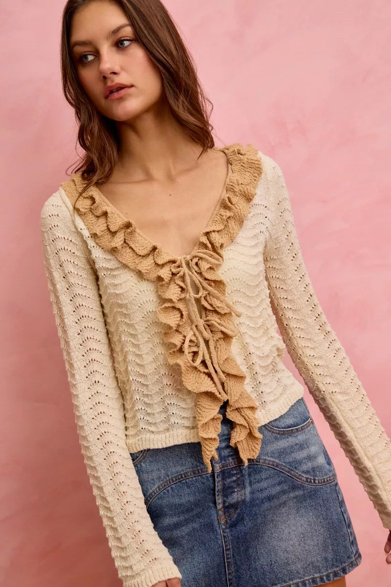 Cream pointelle knit cardigan with ruffled tie-front detail and fitted silhouette.